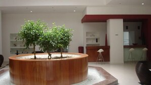A modern lobby with a circular wooden planter containing two trees, a reception desk, and a bar area. - Hotel Bienestar Termas de Monção (Monção)