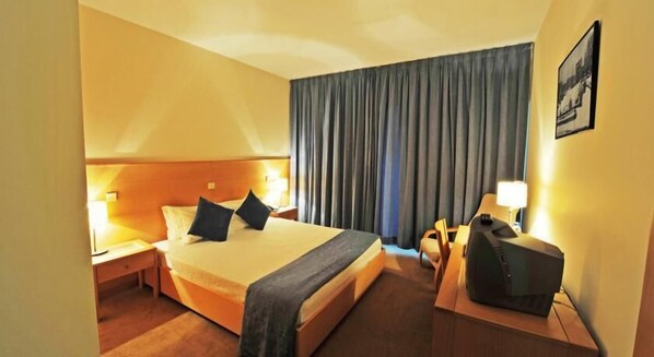 A hotel room with a bed, a desk, a chair, a television, and a window with curtains.