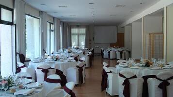 A banquet hall with round tables set for a formal event, featuring white tablecloths and chairs with red sashes.