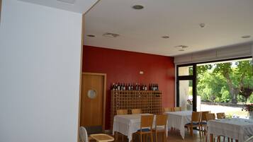 A dining area with tables and chairs, a wine rack, and a view of greenery outside.