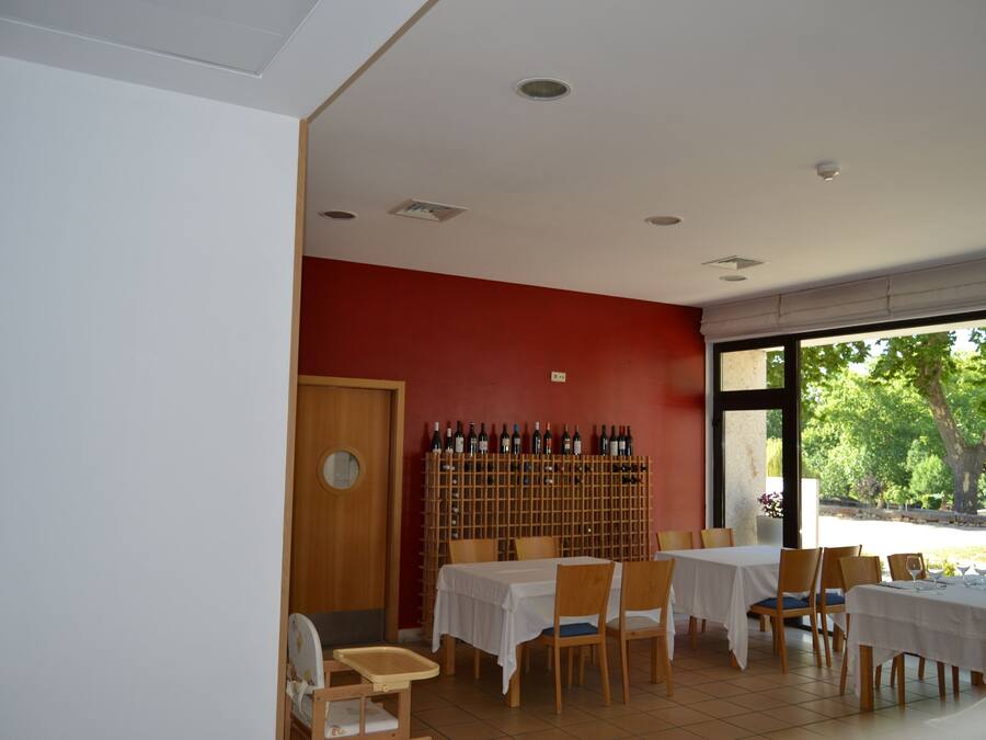 Zona pranzo con tavoli e sedie, una dispensa per vino e vista su del verde all'esterno.