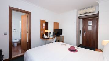 A hotel room with a bed, a television, a desk with a lamp, a mirror, and a door leading to a bathroom.