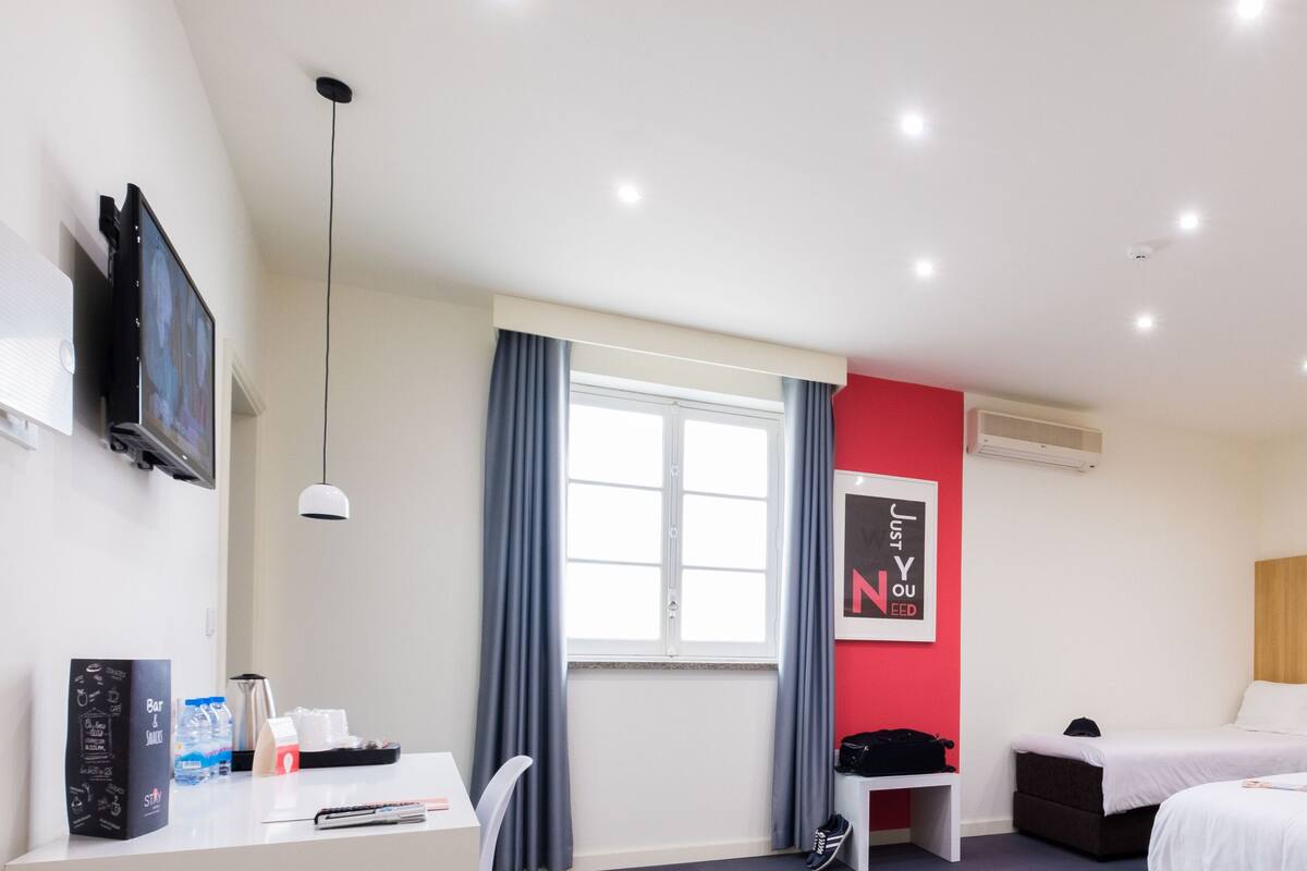 Ein Hotelzimmer mit zwei Betten, einem Schreibtisch, einem Stuhl, einem Fernseher und einem Fenster mit Vorhängen.