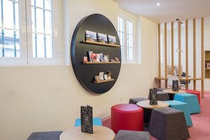 A modern interior with a large black oval wall art piece, multiple seating areas with colorful cushions, and a wooden shelf with books and small items. - Stay Hotel Évora Centro (Évora)