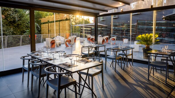 An outdoor dining area with tables and chairs, large windows, and a view of the surrounding area. - Black Hotel (Rome)