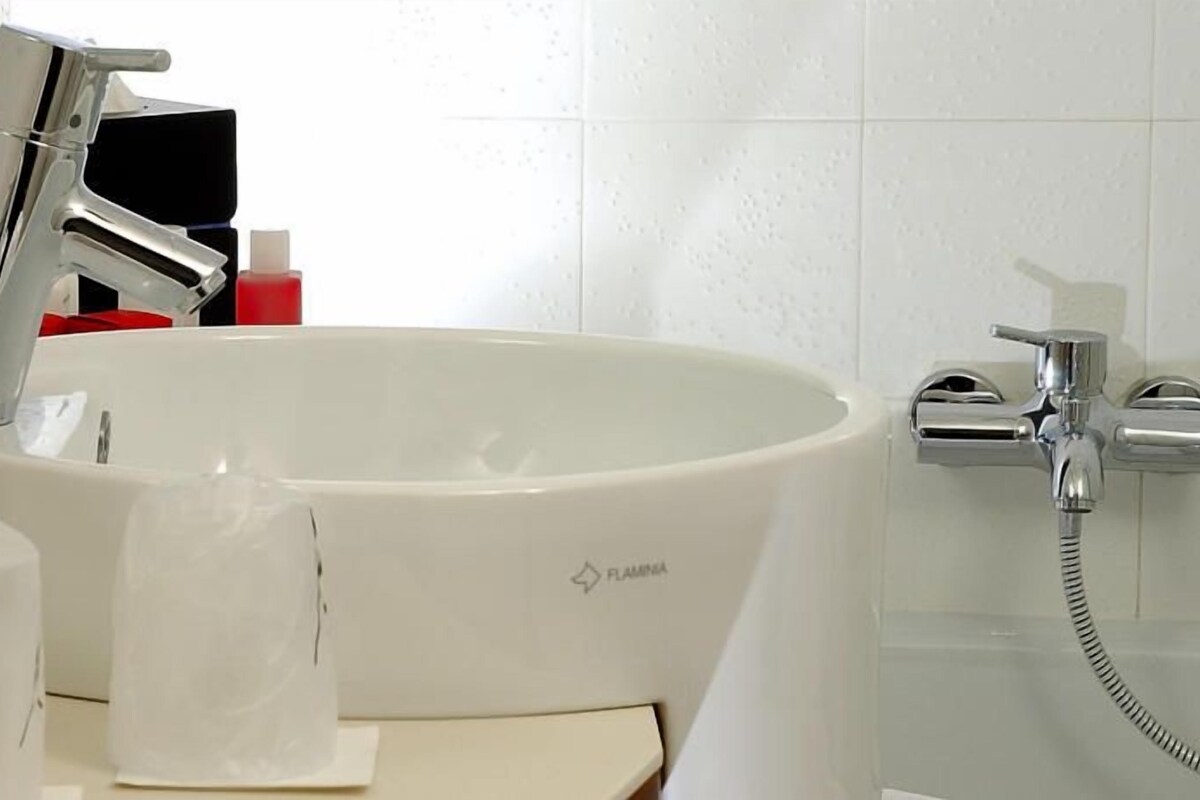 Un baño con lavamanos blanco, grifo cromado y cabezal de ducha de mano.
