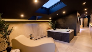 A modern bathroom with a skylight, a curved seating area, a freestanding bathtub, and a potted plant. - Black Hotel (Rome)