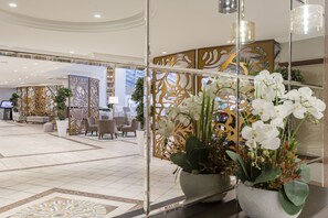 A hotel lobby with a modern design, featuring a seating area with sofas and chairs, decorative panels, and a large potted plant with white flowers. - Papillon Belvil Holiday Village - All Inclusive (Serik)