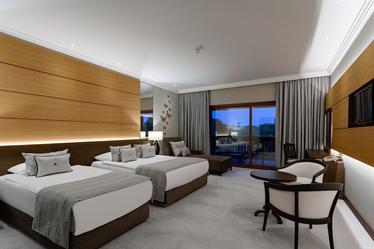 A modern hotel room with two beds, a sitting area, and a balcony with a view.