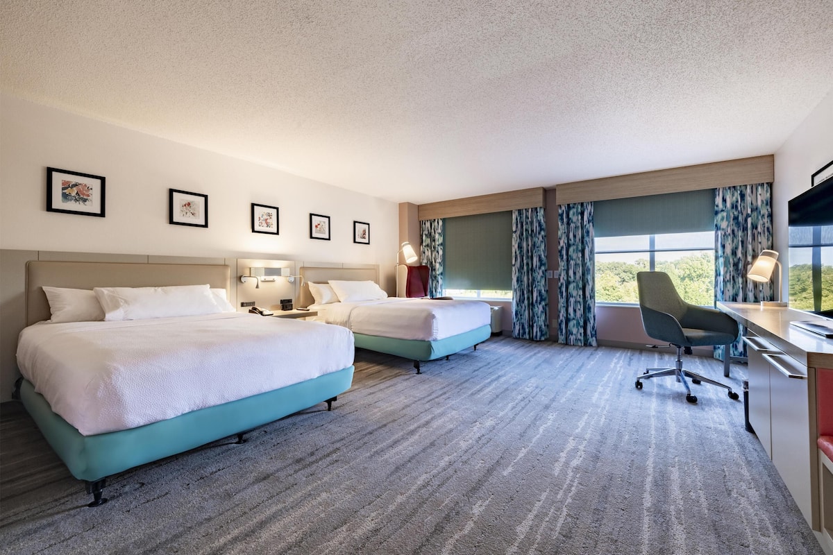 A hotel room with two beds, a desk, a chair, and a TV.