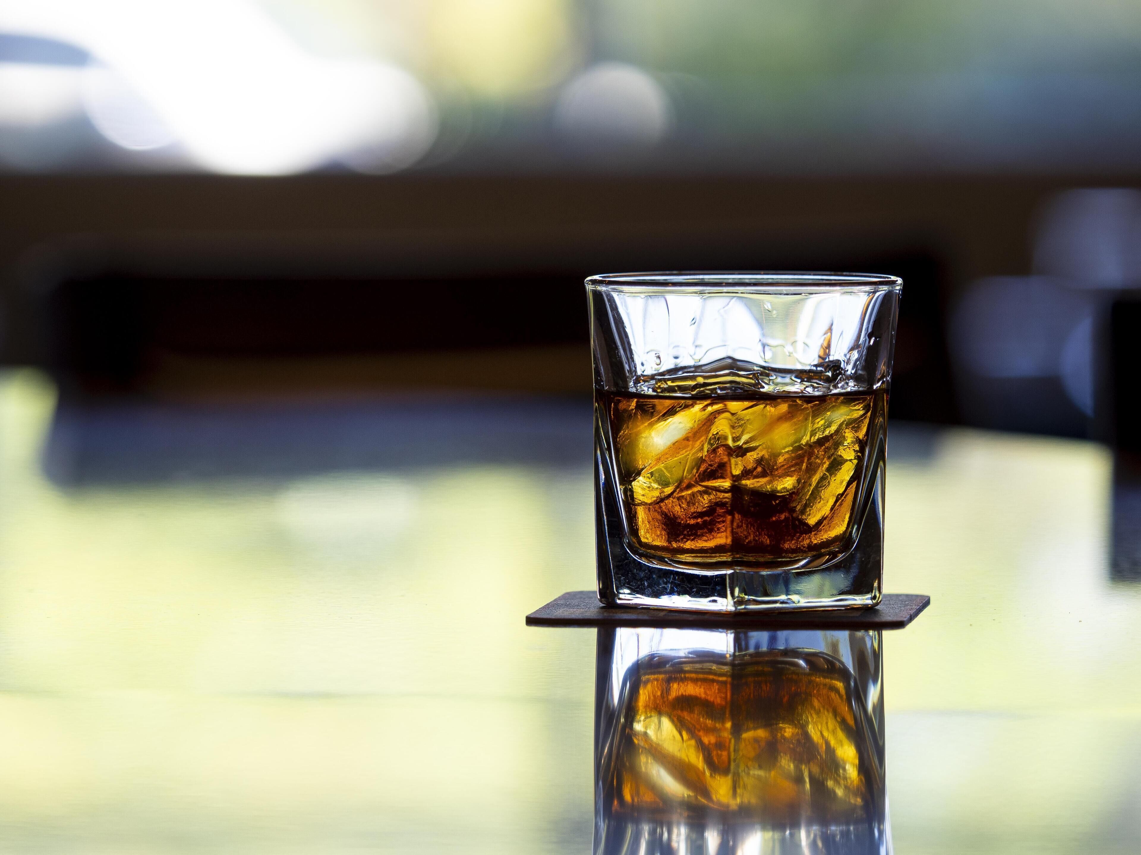 Ett glas med en bärnstensfärgad vätska står på en reflekterande yta, med en suddig bakgrund.