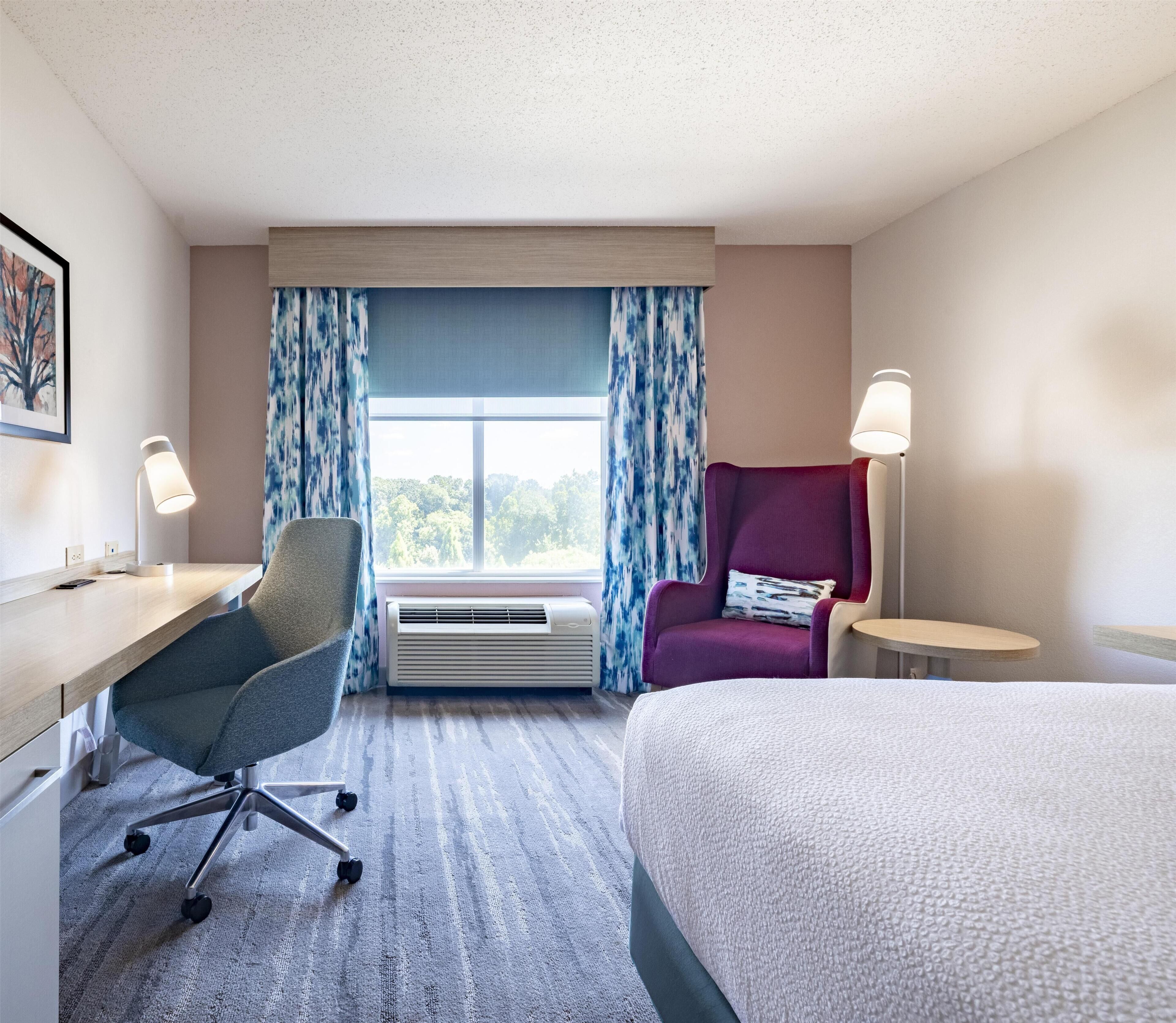 A hotel room with a desk, chair, bed, and two bedside lamps.