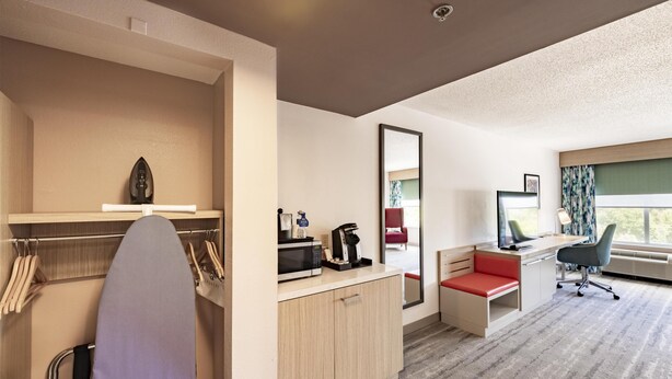 A hotel room with a bed, a desk, a chair, a mirror, and a window with curtains.