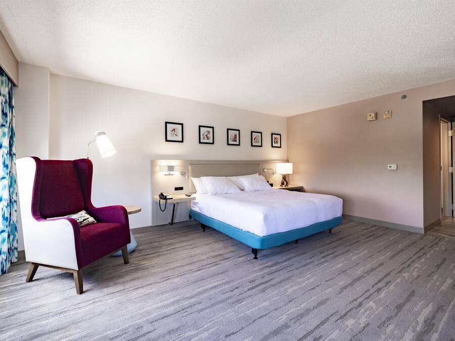 Una camera d'hotel con un letto, una poltrona rossa, una scrivania e un comodino.