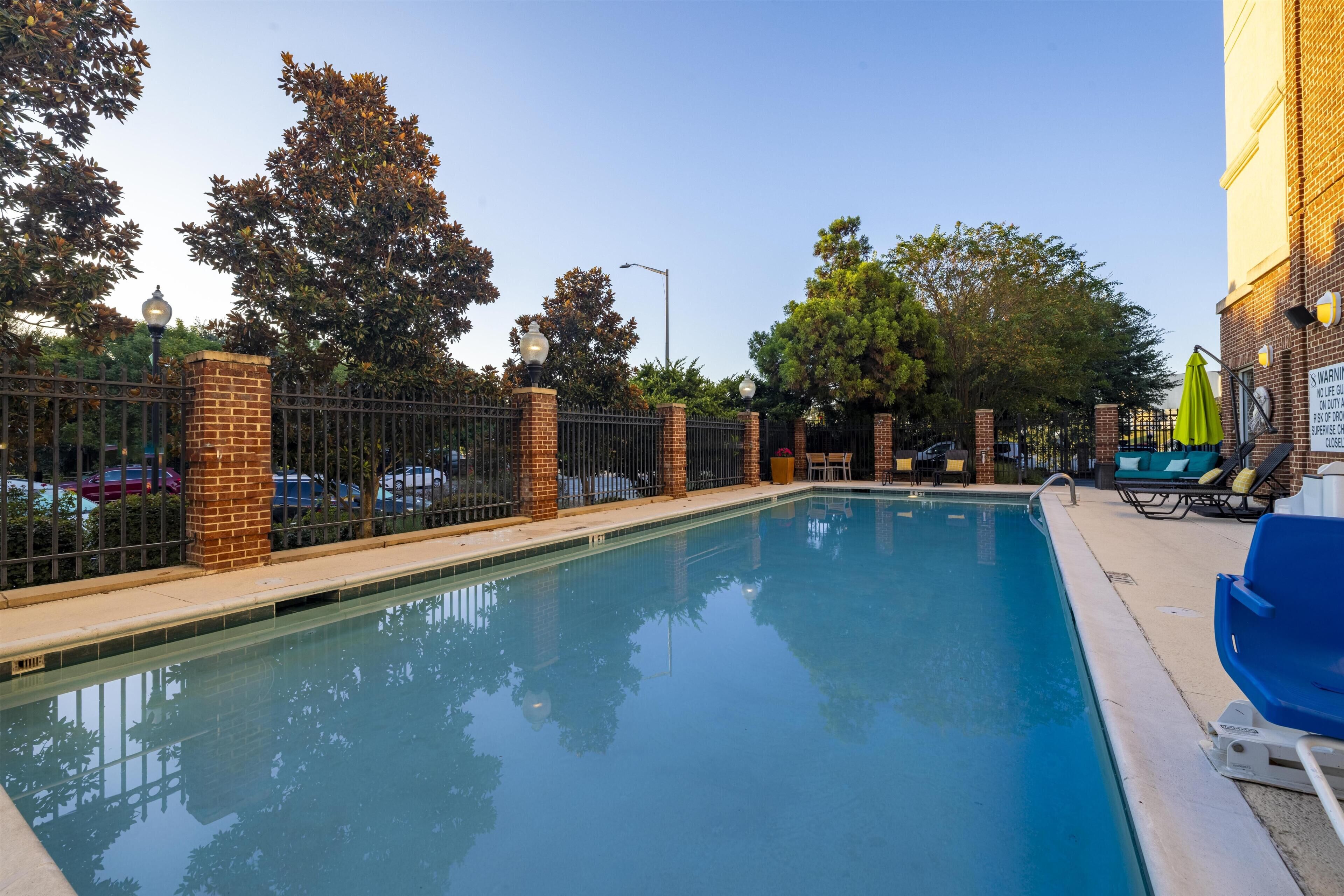 A swimming pool with a brick wall, metal fence, and lounge chairs.