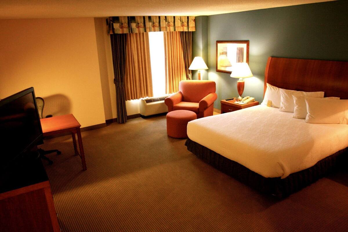A hotel room with a bed, a desk, a chair, a lamp, and a picture on the wall.
