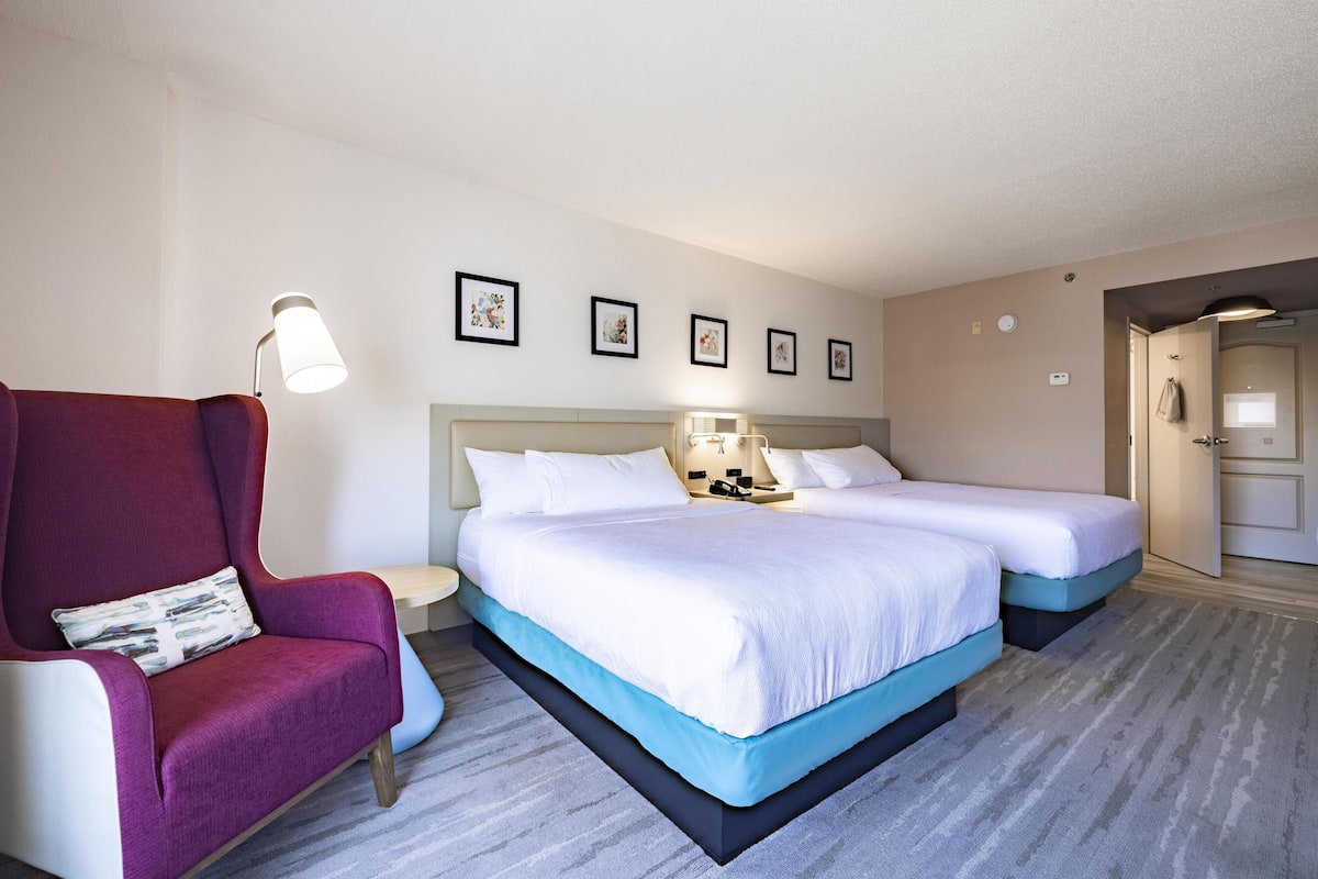 A hotel room with a large bed, a chair, a nightstand, and a wall with framed pictures.