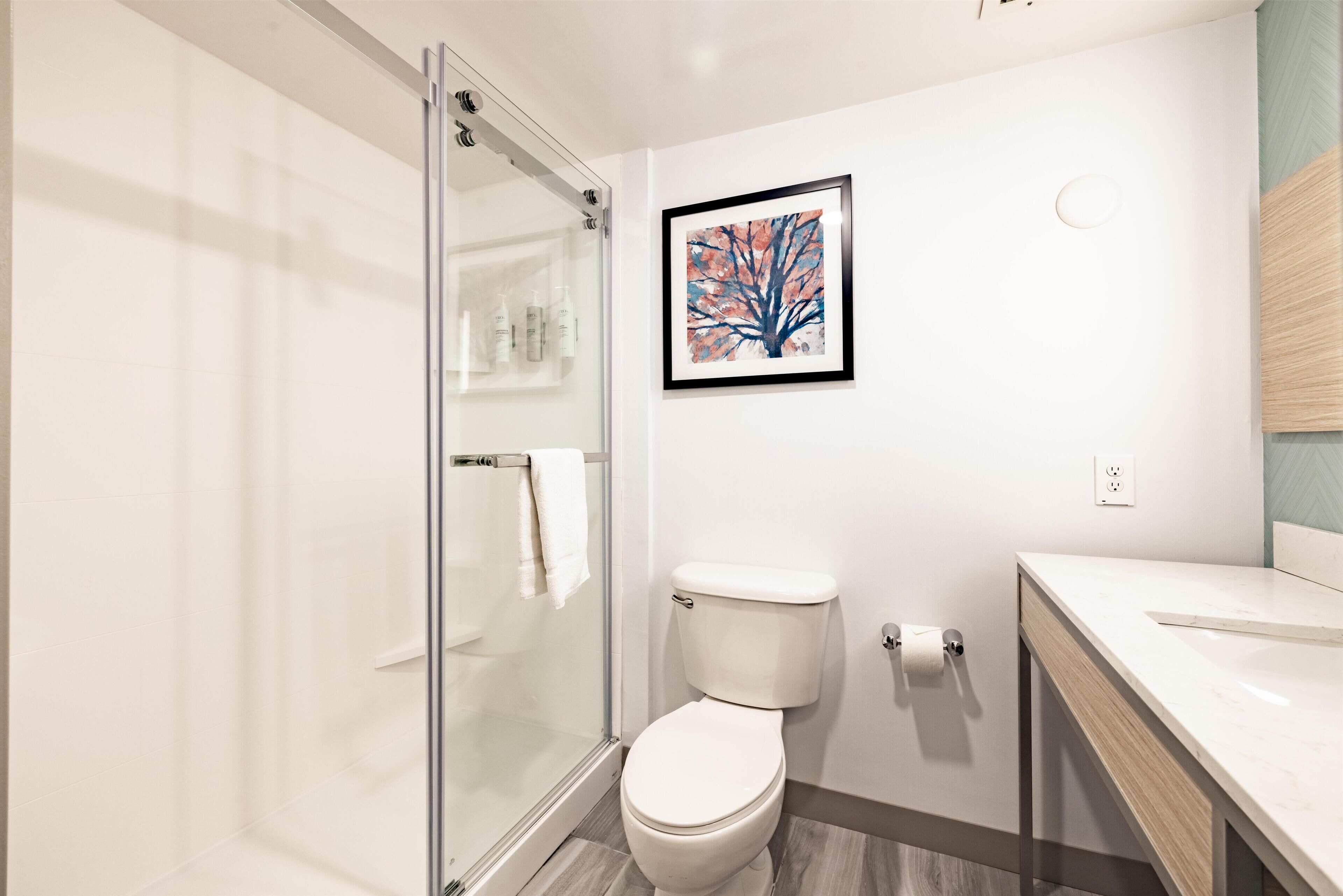 A modern bathroom with a glass shower enclosure, a toilet, and a sink with a wooden countertop.