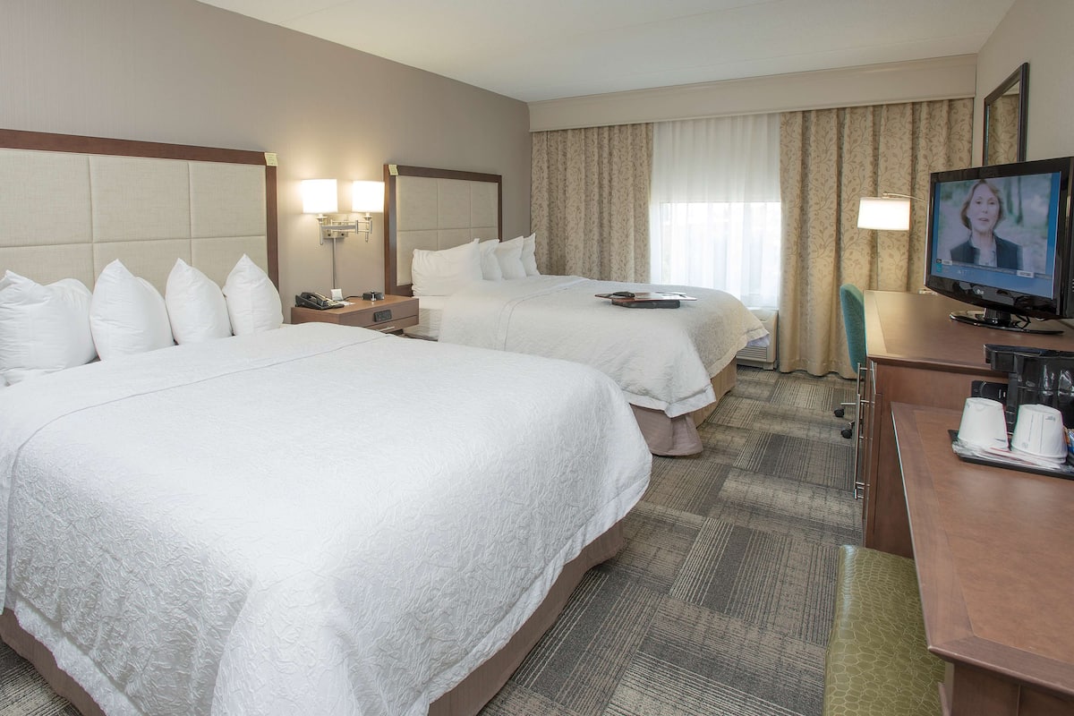 A hotel room with two beds, a desk with a computer, and a TV.