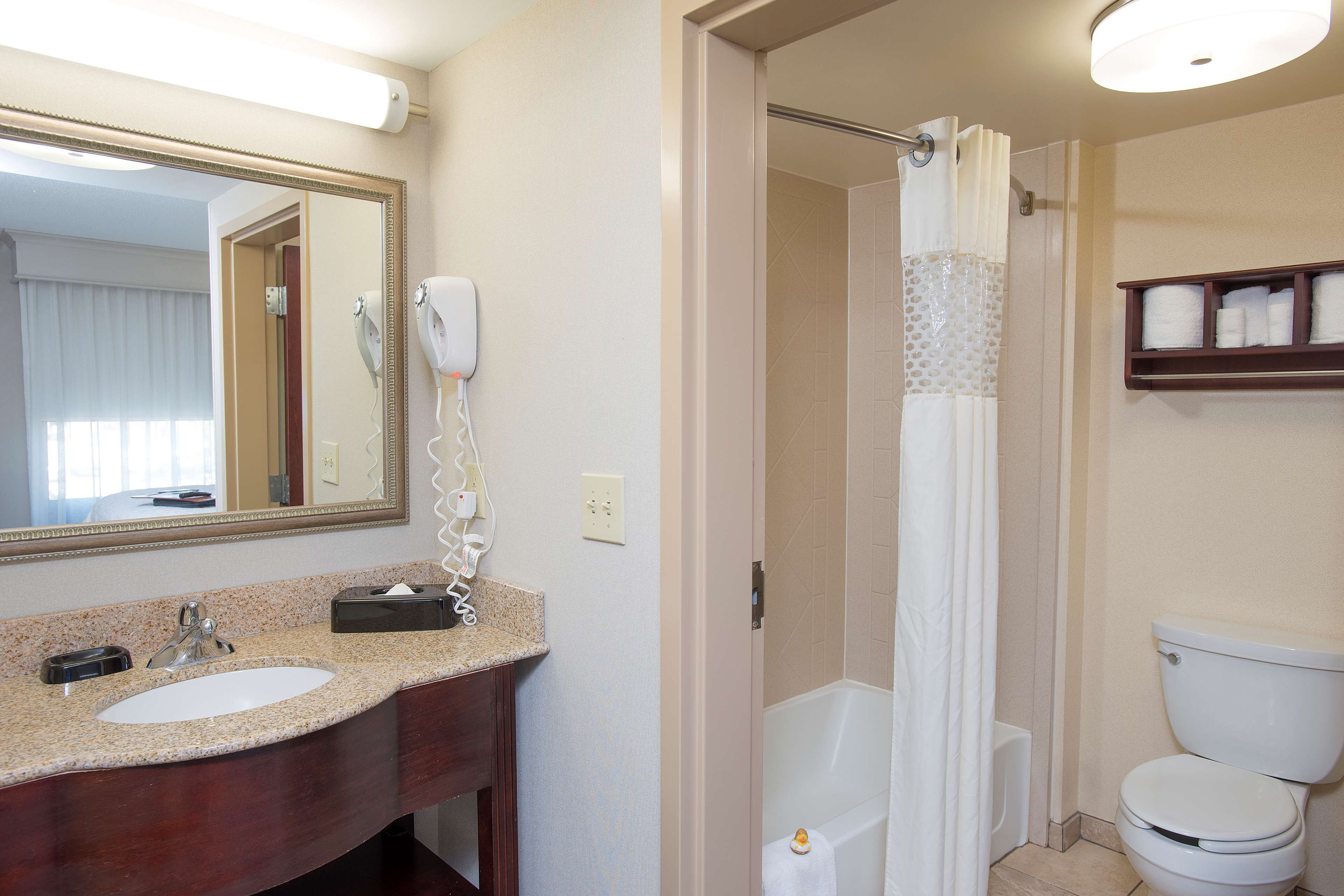 A bathroom with a sink, mirror, hairdryer, and a shower curtain.