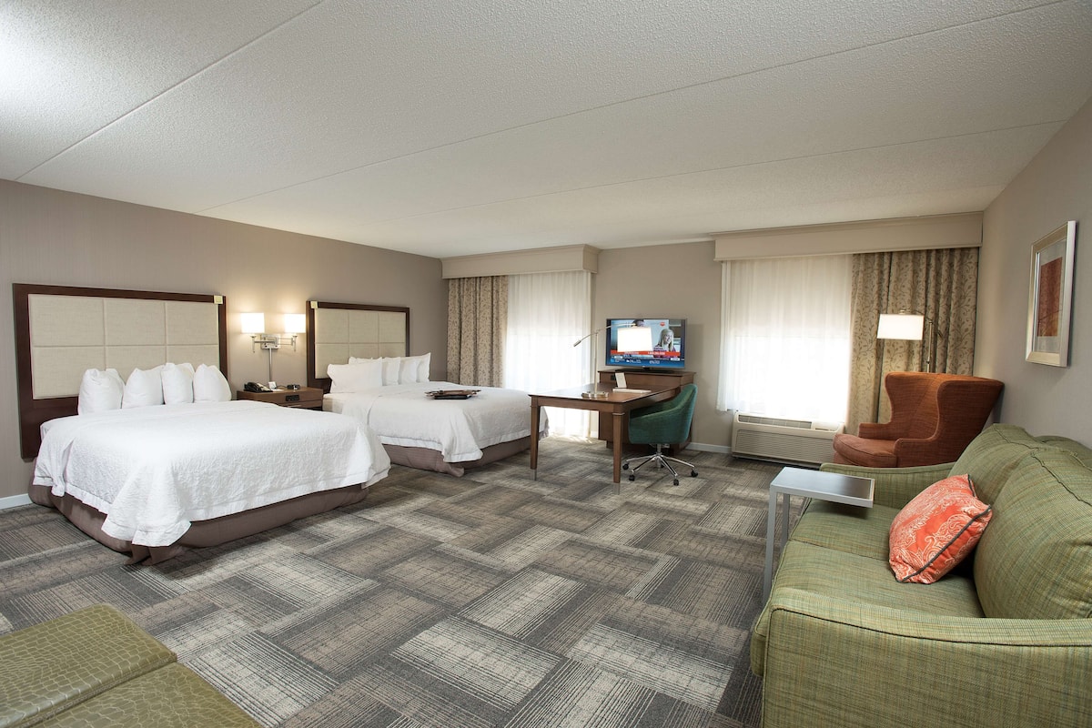 A hotel room with two beds, a desk, a television, and a green sofa.