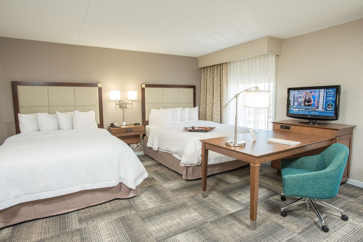 A hotel room with two beds, a desk, a television, and a chair.