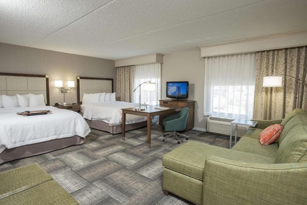 A hotel room with two beds, a desk, a television, a sofa, and a lamp.