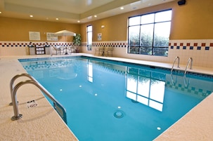 Piscina interior com água cristalina, placas de segurança e parede revestida de azulejos.