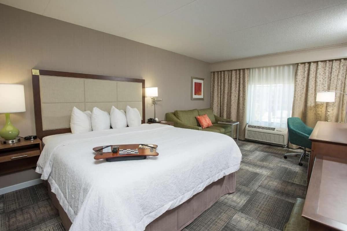 A hotel room with a large bed, a desk, a chair, a sofa, and a window with curtains.
