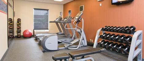 A gym with treadmills, ellipticals, a bench press, a red exercise ball, and a rack of dumbbells.