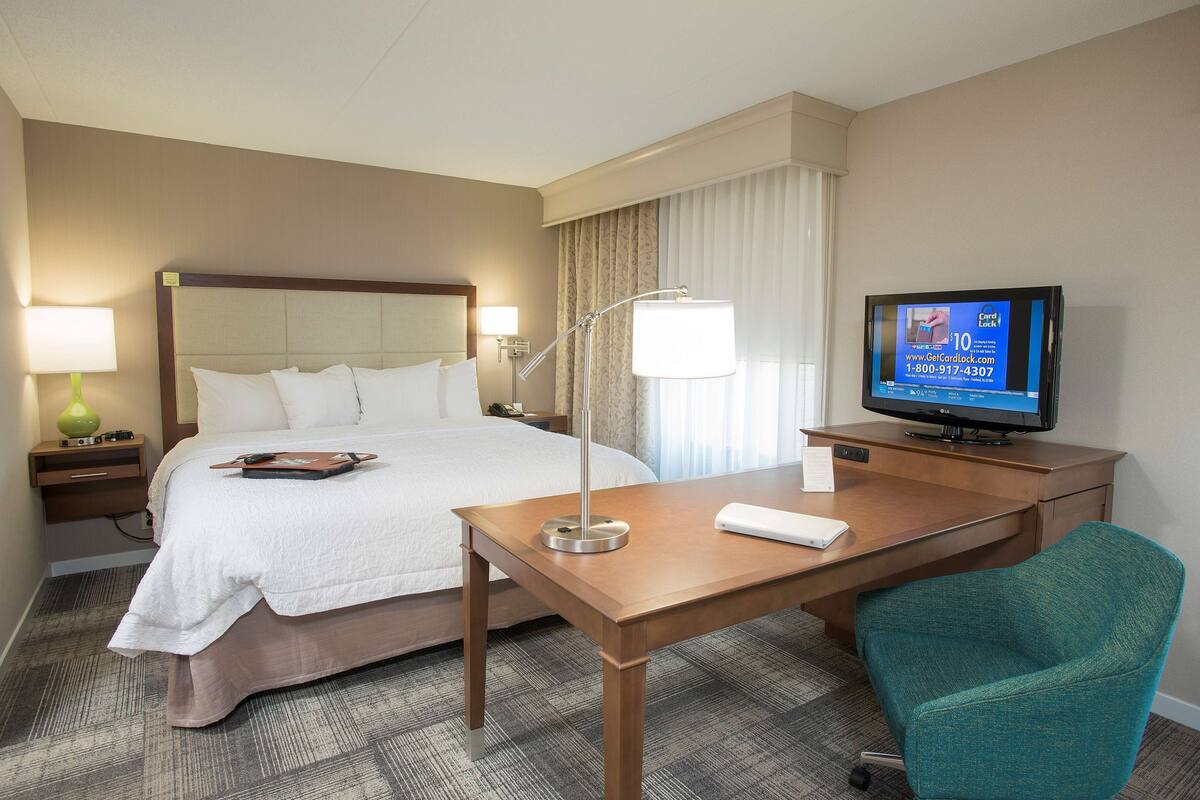 A hotel room with a bed, a desk, a television, a chair, and a lamp.