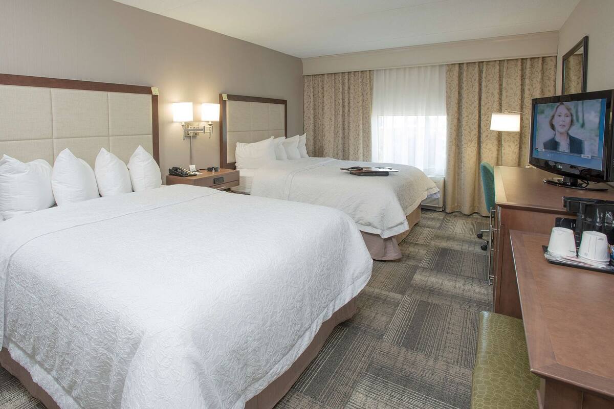 A hotel room with two beds, a desk with a computer, and a TV.