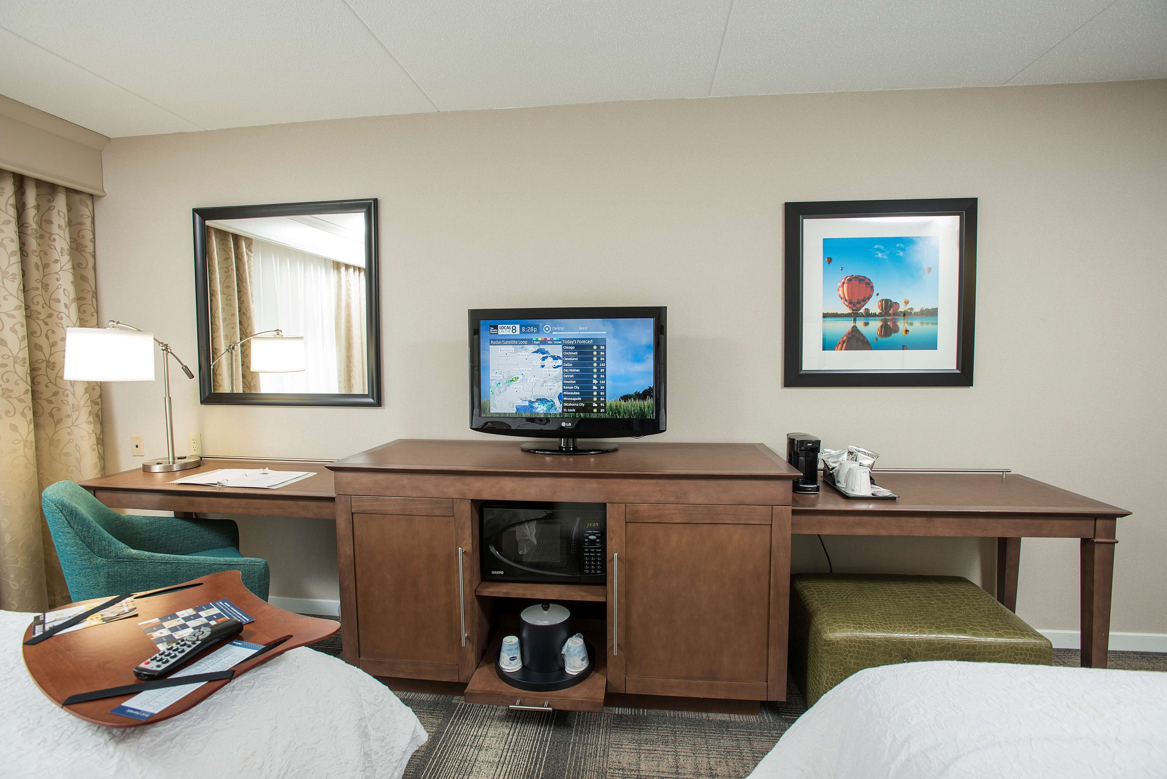 Habitación de hotel con cama, escritorio, televisor, microondas y cafetera.