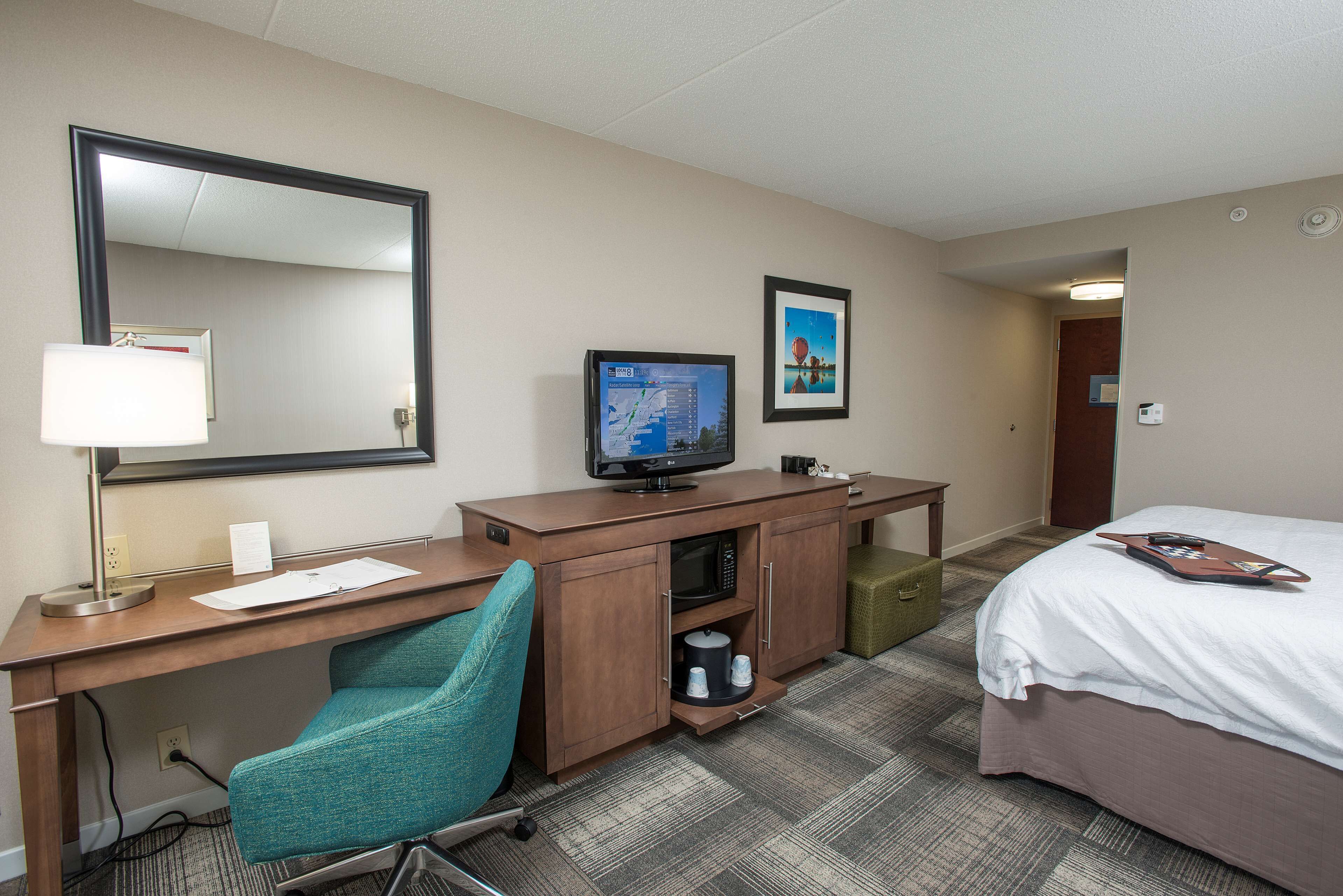 A hotel room with a desk, chair, television, bed, and a small cabinet.