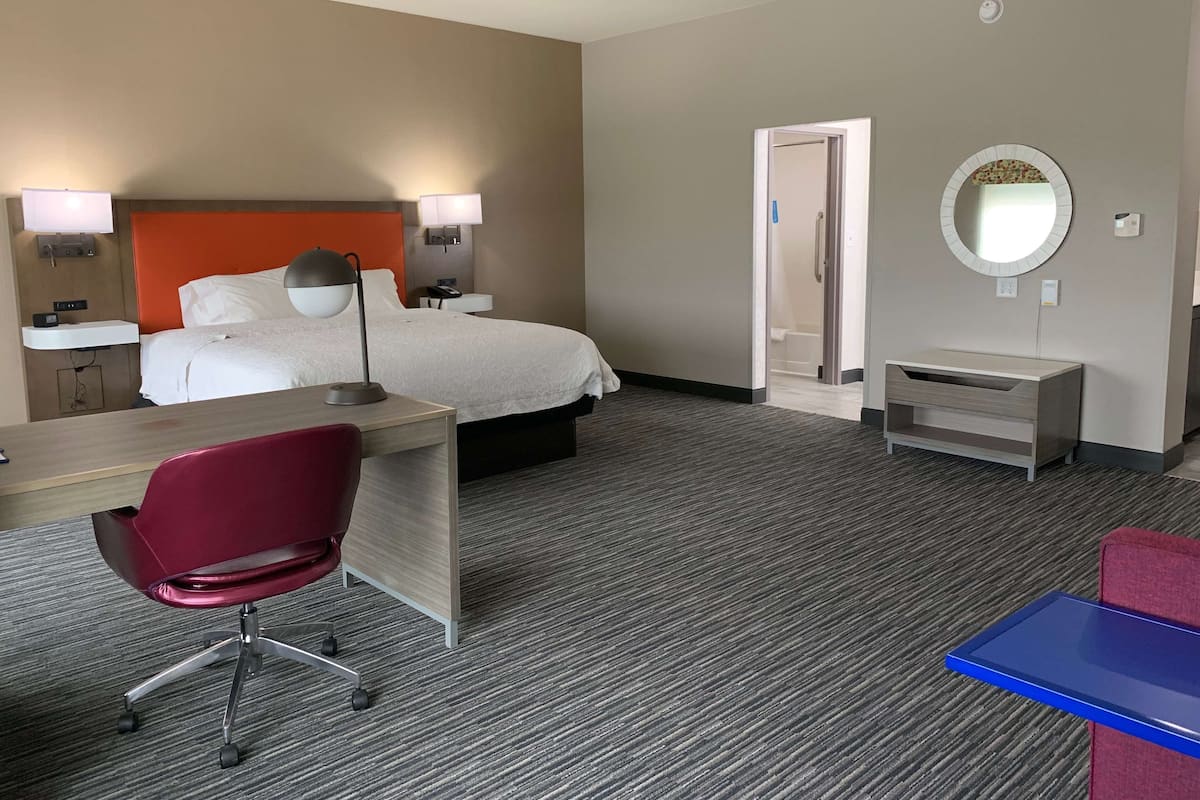 A hotel room with a bed, desk, chair, and a small table with a mirror.