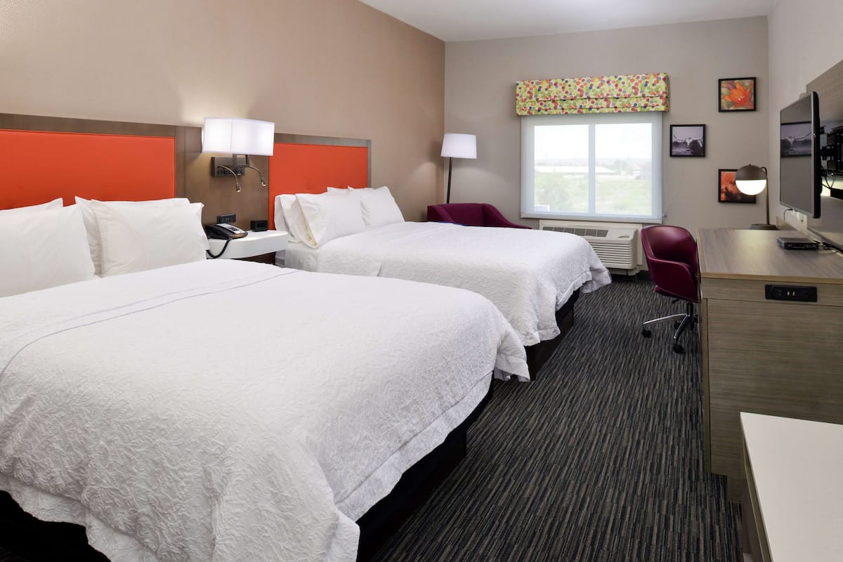 A hotel room with two beds, a desk, a chair, a TV, and a window with a view.