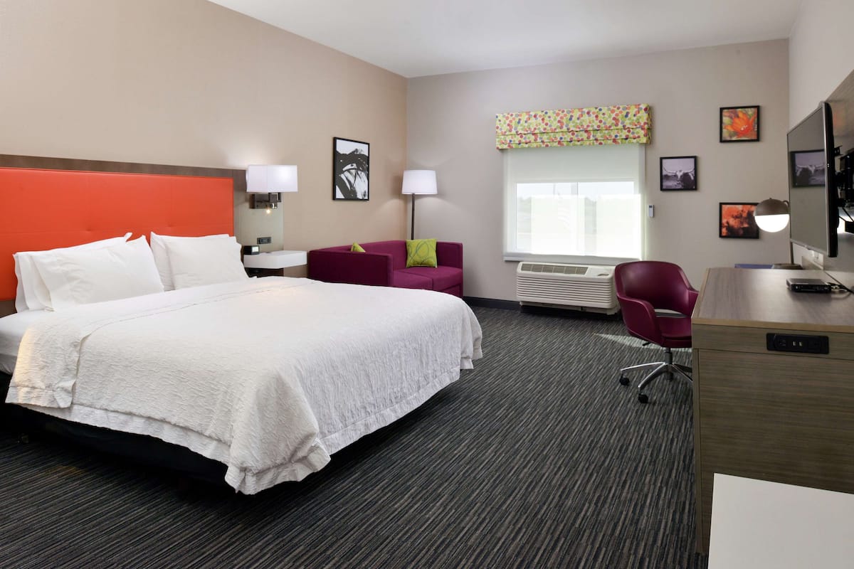A hotel room with a large bed, a desk, a chair, and a window with a view.