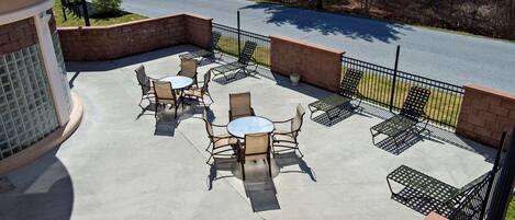 An outdoor patio area with tables and chairs, surrounded by a brick wall and metal fencing.