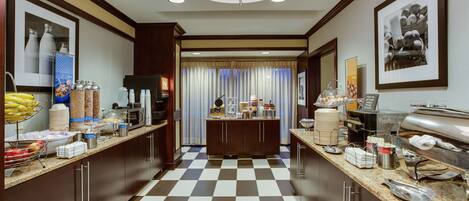 A hotel kitchen with checkered flooring, stainless steel appliances, and various food items on counters.