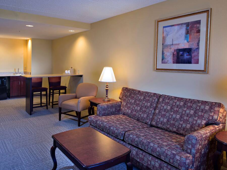 Une chambre d’hôtel comprenant un canapé, deux fauteuils, une petite table, une lampe, un four à micro-ondes et un coin cuisine avec un évier et un plan de travail.
