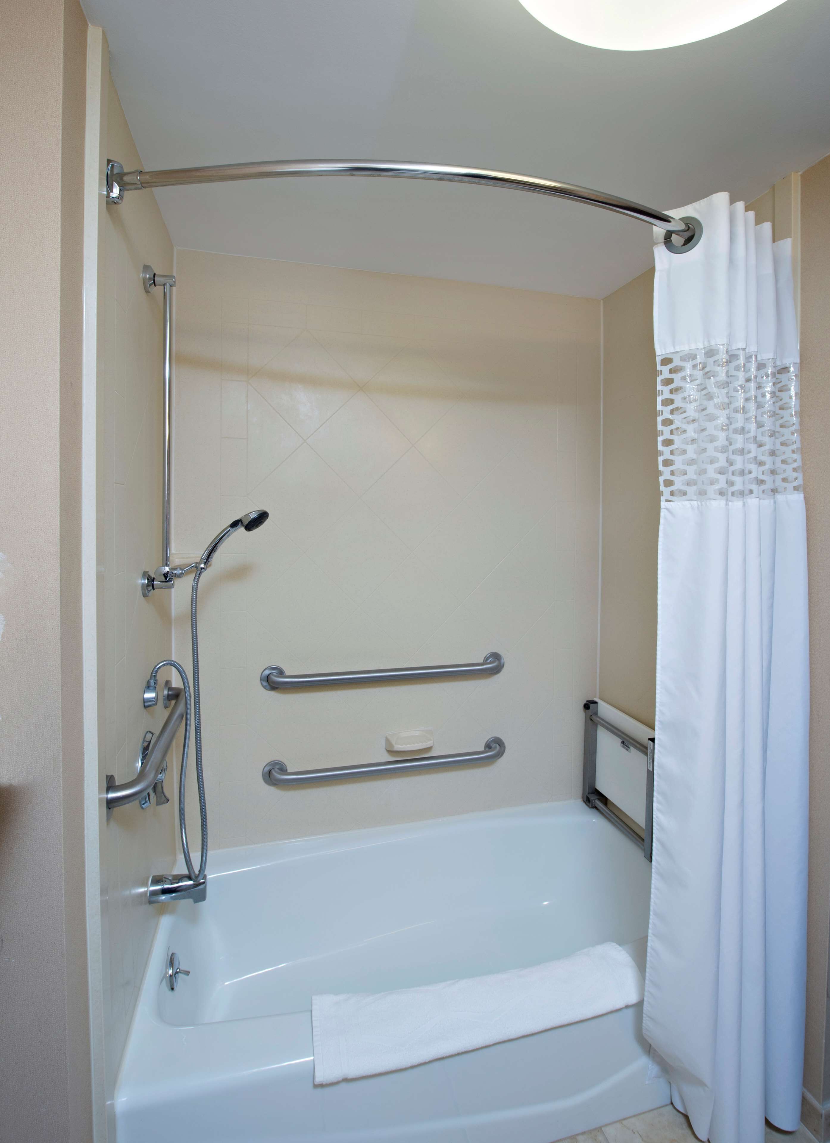 Un baño con cabina de ducha, barras de apoyo, una bañera blanca y un cortinón de ducha blanco.