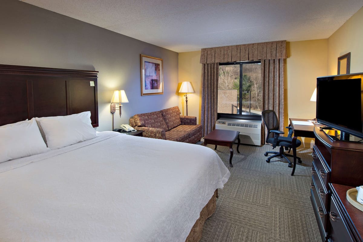 A hotel room with a large bed, a sofa, a desk with a television, a coffee maker, and a window with curtains.