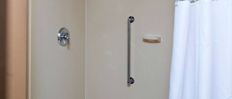A walk-in shower with a glass door, a handheld showerhead, a handheld shower control, a grab bar, and a white shower curtain.