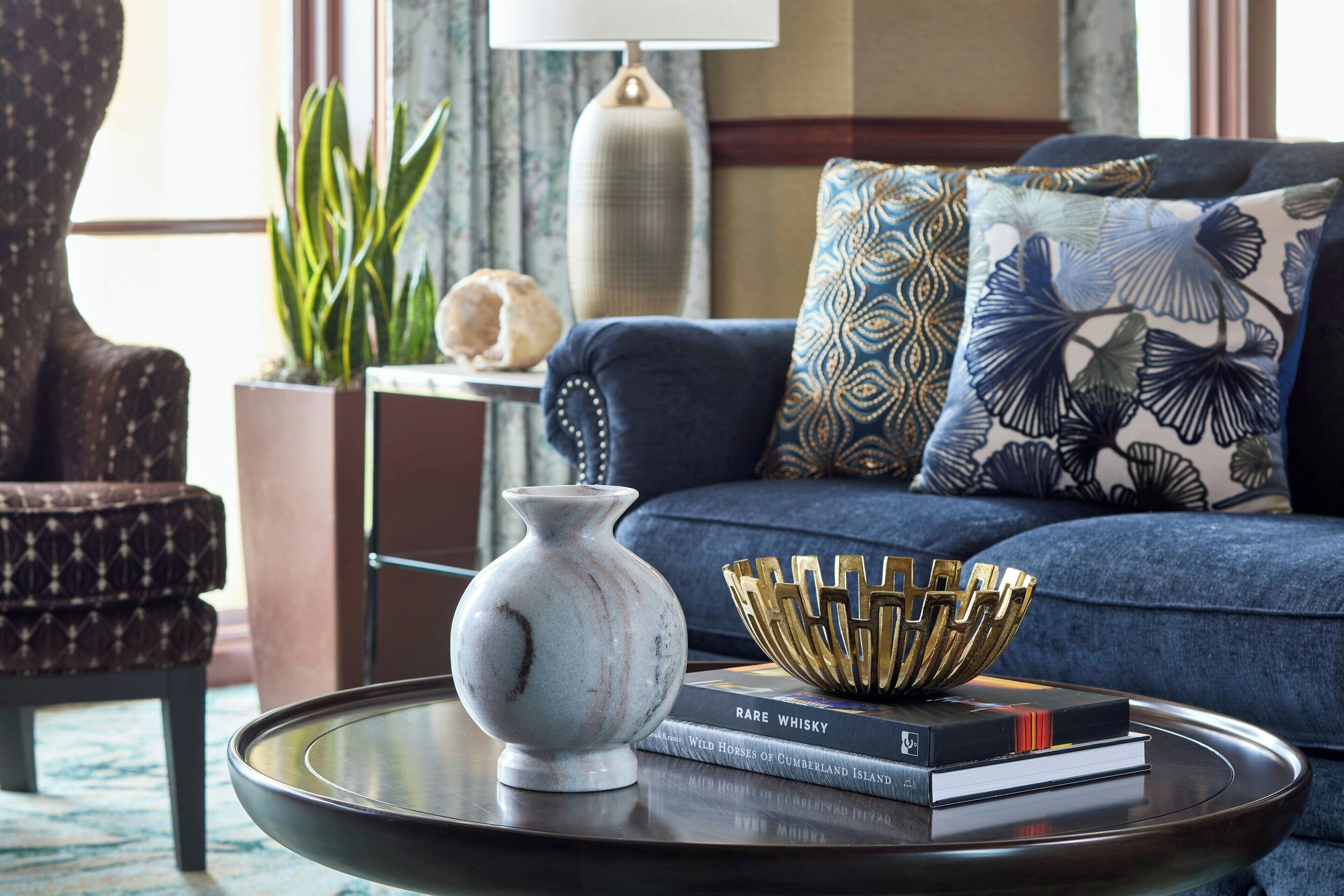 Una sala de estar moderna con un sofá, almohadones decorativos, un florero, un cuenco y libros sobre una mesa de centro de vidrio.