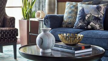 Una sala de estar moderna con un sofá, almohadones decorativos, un florero, un cuenco y libros sobre una mesa de centro de vidrio.