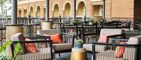 An outdoor seating area with multiple tables and chairs, surrounded by brick walls and columns.