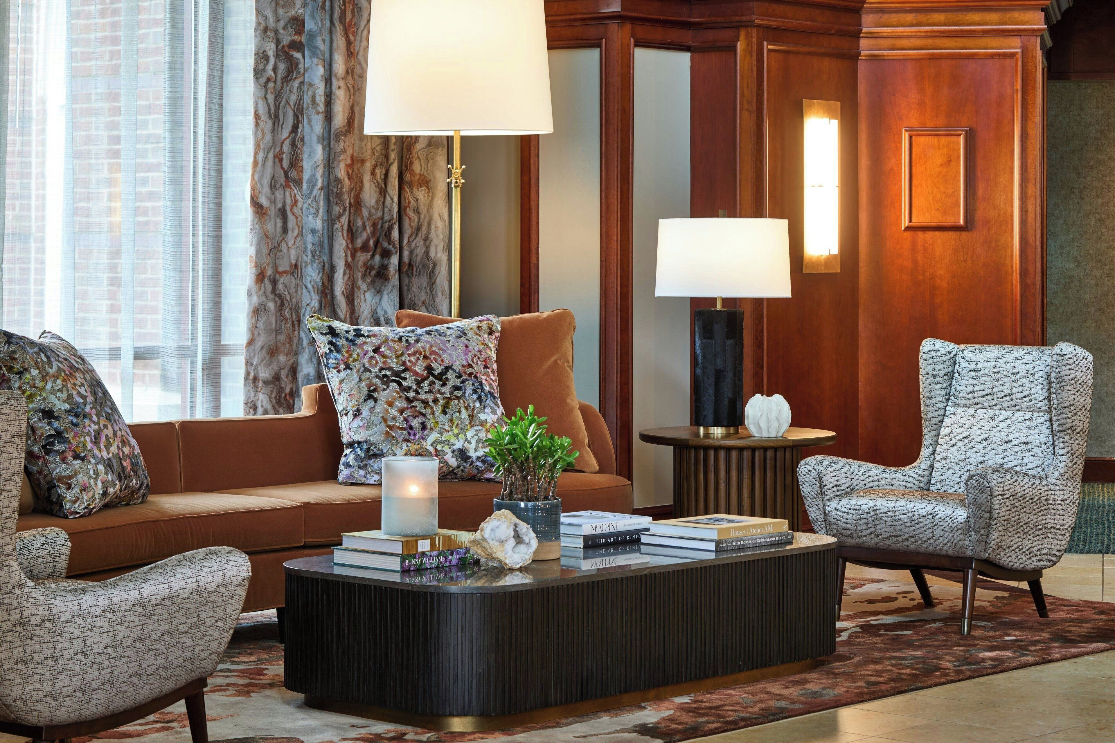 A modern living room with a sofa, two armchairs, a coffee table with books, a lamp, and a decorative plant.