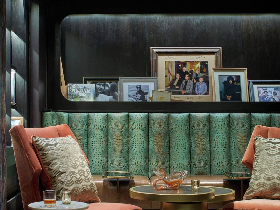 A modern lounge area with two plush armchairs, a round gold table, and a green patterned bench.