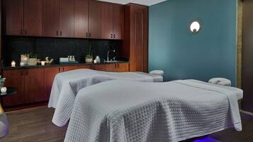 Una spa con due lettini, armadietti in legno, un lavabo e un piccolo tavolo con piante e candele.