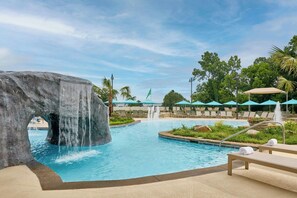 A pool area with a waterfall feature, lounge chairs, and umbrellas.